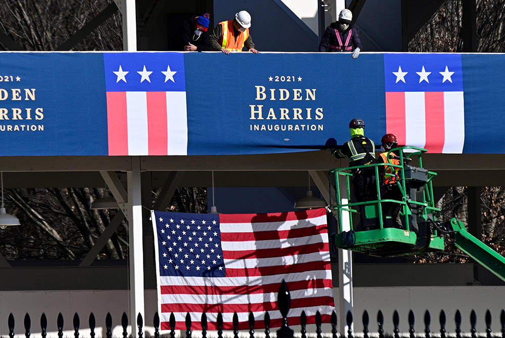 Workers in Washington place Biden-Harris inauguration banners on the inaugural parade viewing stand across from the White House Jan. 14. (CNS/Erin Scott, Reuters)