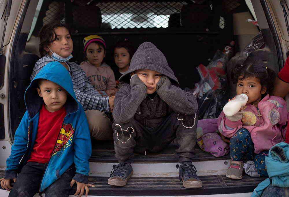 Migrant children from Central America take refuge from the rain in the back of a U.S. Border Patrol vehicle in Penitas, Texas, March 14, as they await to be transported after crossing the Rio Grande into the United States. (CNS/Reuters/Adrees Latif)