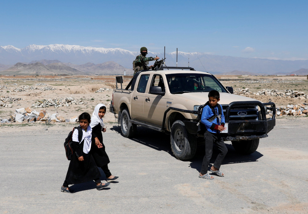 Schoolchildren walk past an Afghan National Army soldier keeping watch at a checkpoint on the outskirts of Kabul, Afghanistan, April 21, 2021. (CNS/Reuters/Mohammad Ismail)