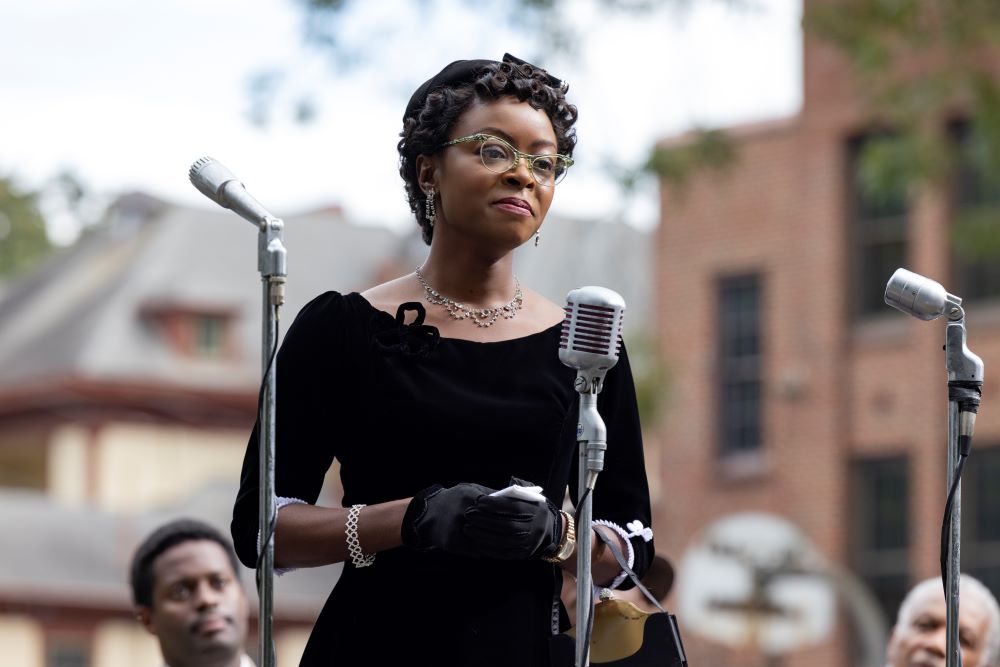 Actress portrays Mamie Till-Mobley, who is standing at a microphone. 