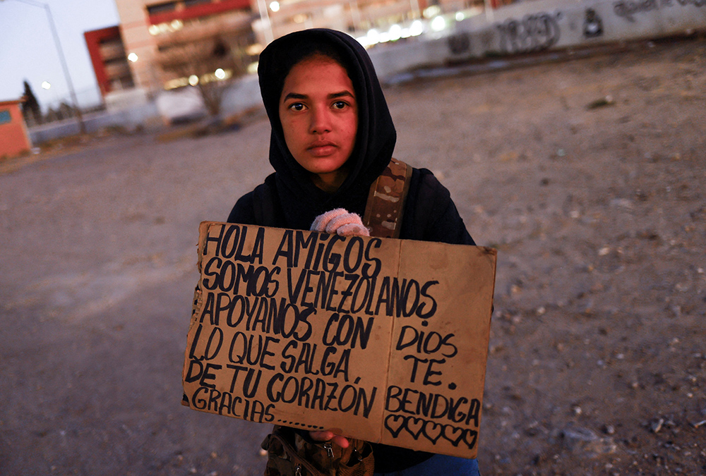 Yalimar Chirinos, a 19-year-old migrant from Venezuela, displays a sign near the U.S.-Mexico border Jan. 7 in Ciudad Juarez, Mexico. The sign reads "Hello friends, we are from Venezuela, support us with what comes out from your heart." (OSV News/Reuters/Jose Luis Gonzalez)