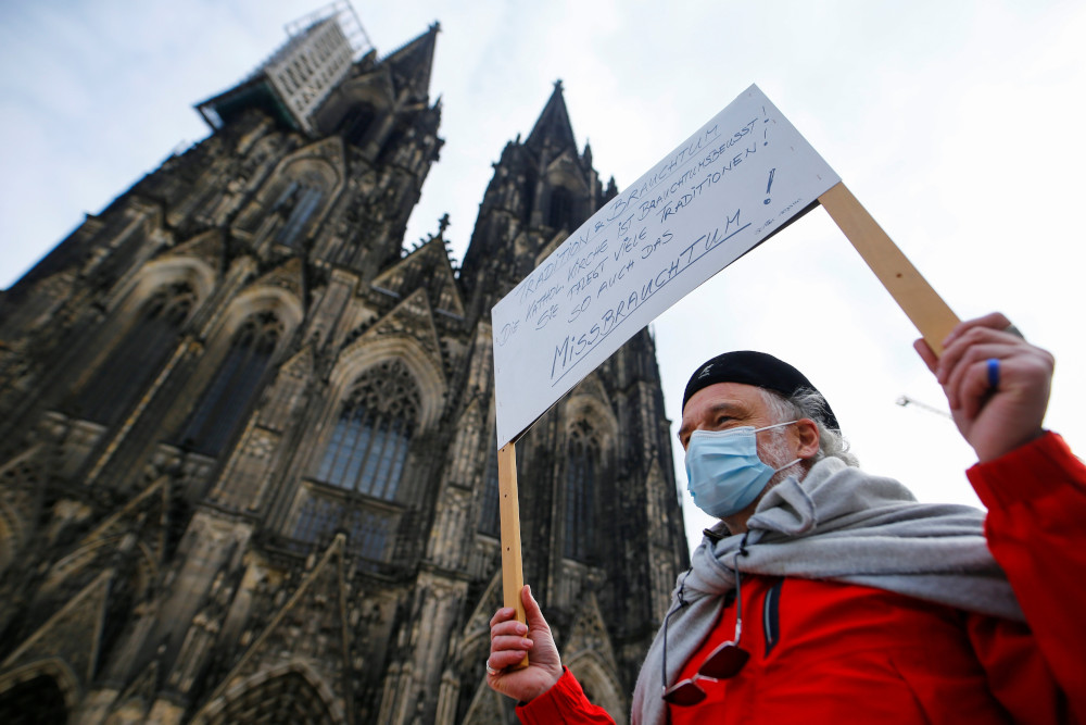 An older person carries a sign and wears a mask outside a cathedral