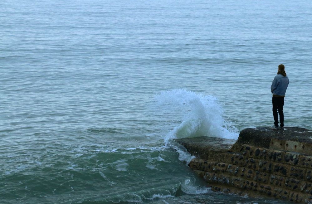 A man stands on a rock looking out over the ocean (Unsplash/Pierre Bamin)