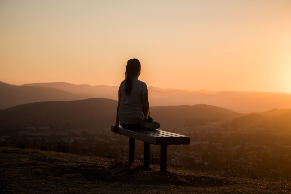 Woman sitting on bench looking out over mountain range (Unsplash/Sage Freidman)