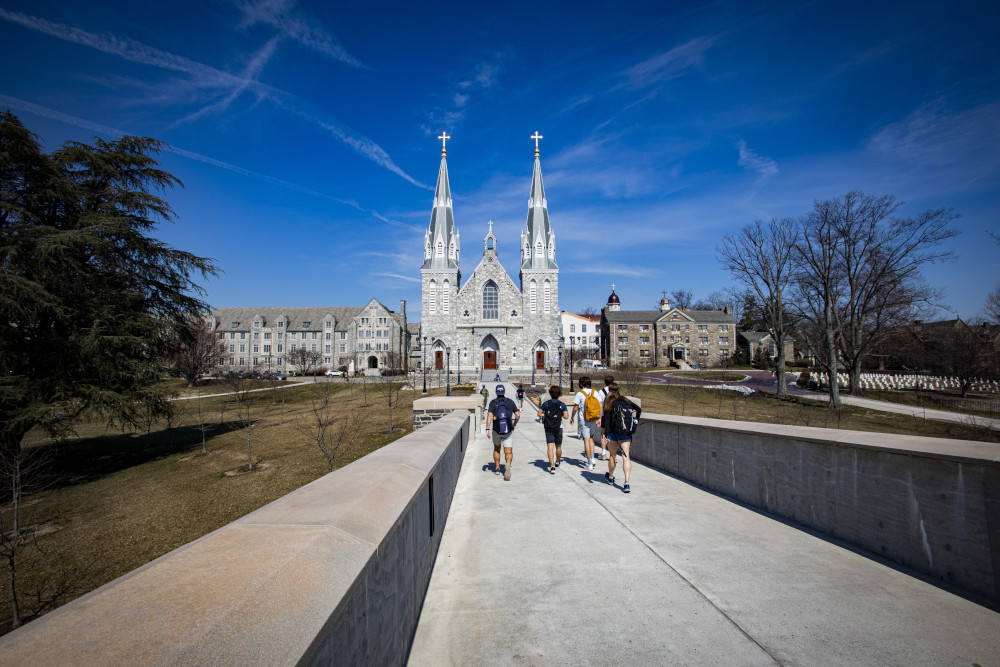 Young adults with backpacks walk down a sidewalk towards a church with two spires