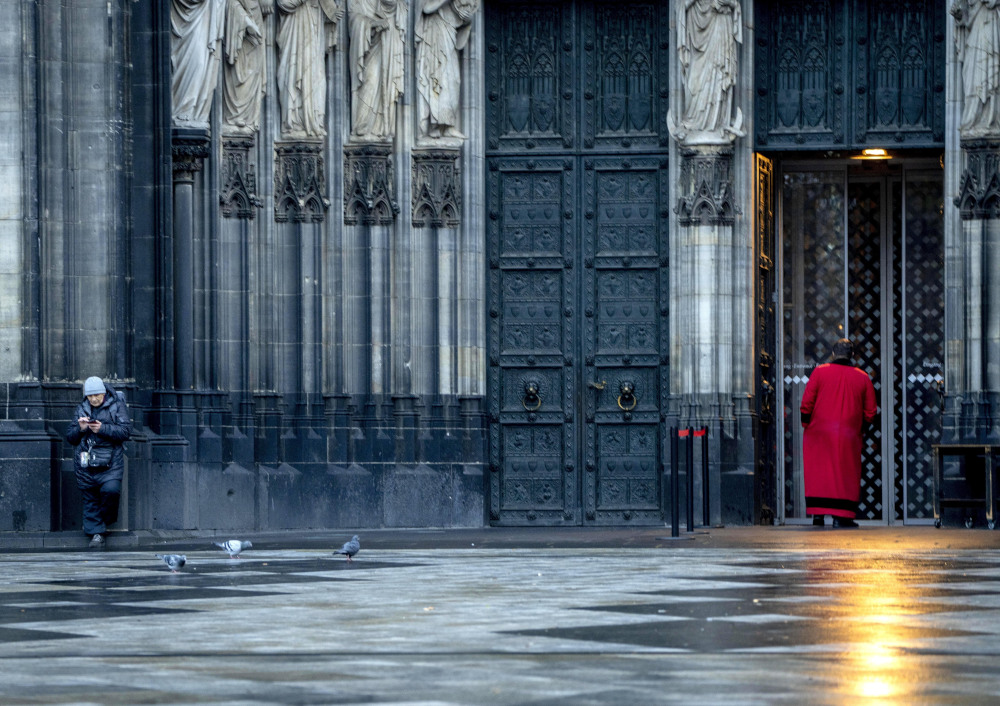 Two people are outside a cathedral with statues and ornate doors in a shiny square with pigeons