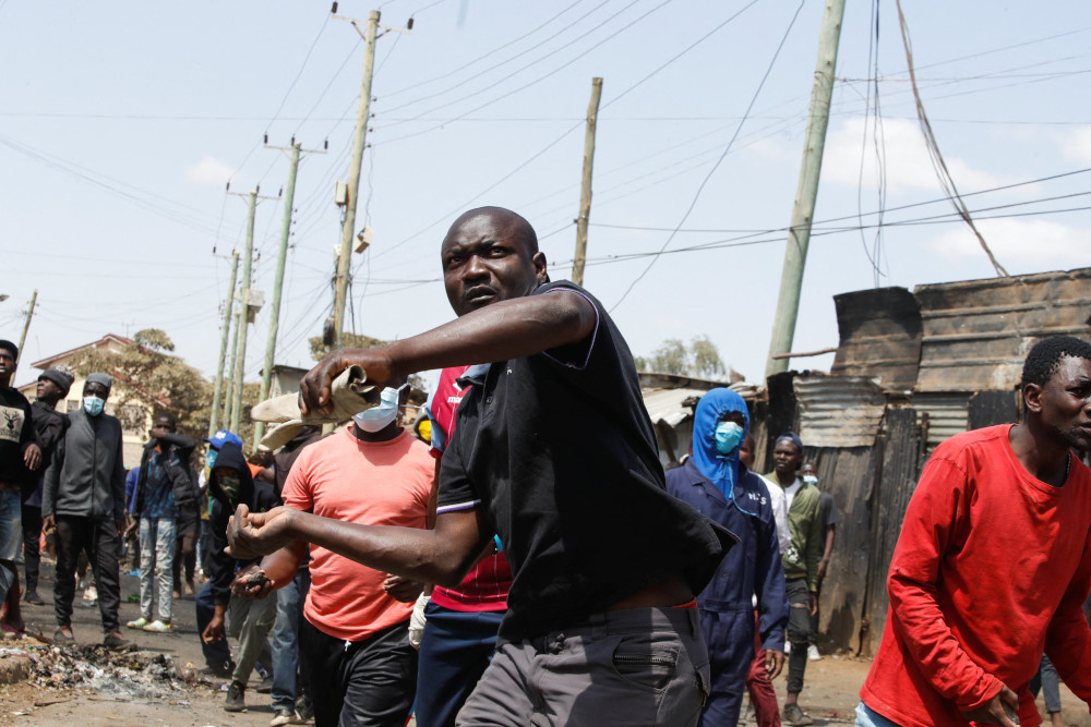 A Black man holds his hands back while carrying a rolled up paper. Other Black men, many wearing surgical masks, surround him.