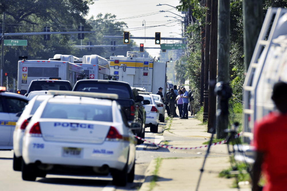 A police vehicle and other emergency vehicles are visible along a sidewalk where a small group of people are gathered