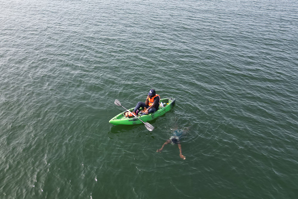 A member of the Agbetsi Living Water Swim expedition crew radios other crew members with a status update while paddling alongside Yvette Tetteh as she swims in the Volta River in Ghana. (Courtesy of the Or Foundation)