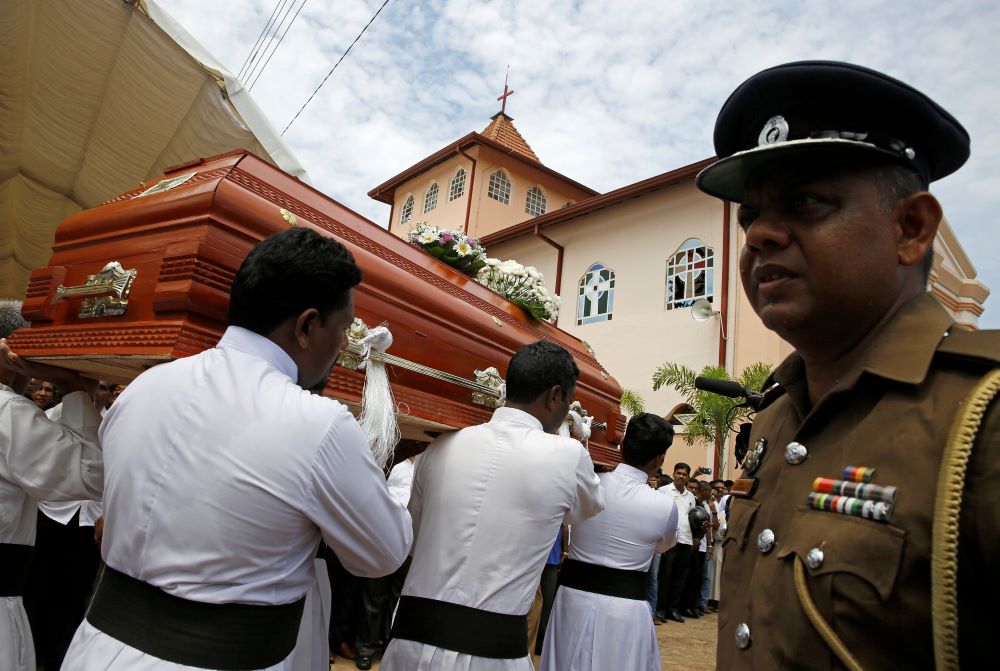 Member of military stands as pallbearers wearing white carry coffin.