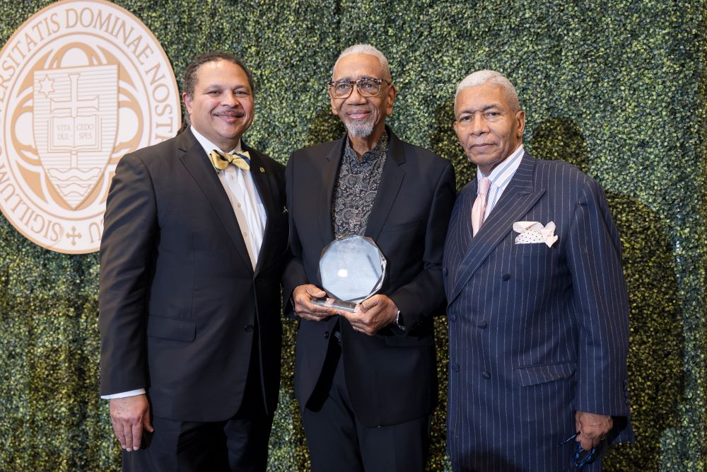 Three men, with one in center holding an award.