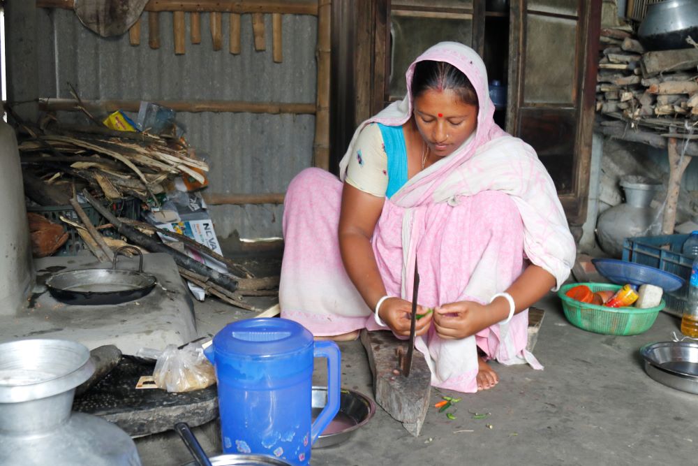 Woman crouches on ground and cooks.