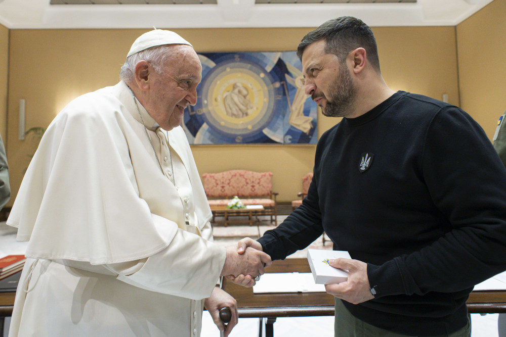 Pope Francis shakes hands with President Volodymyr Zelenskyy shake hands in a yellow room