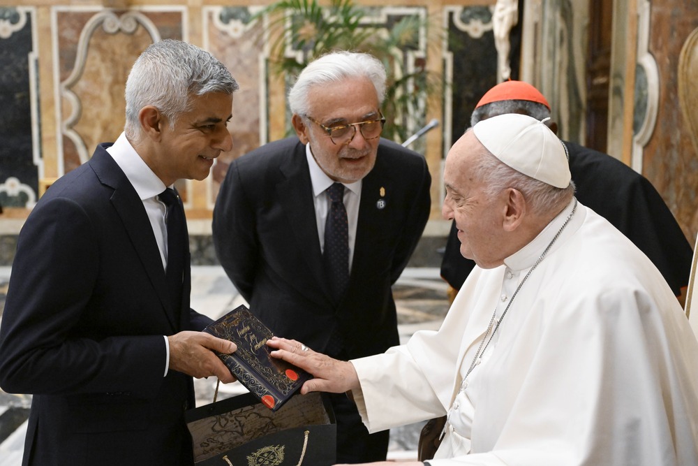 Pope, seated, smiles amid discussion with standing mayor. 