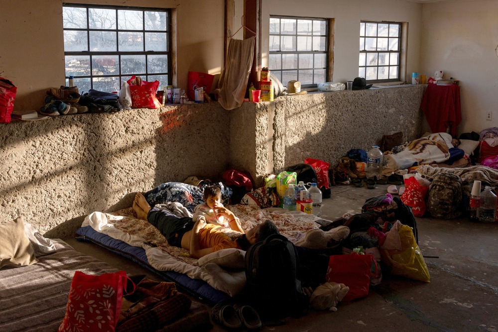 Man and girl lay on mattress in a sun-lit, earthen room. 