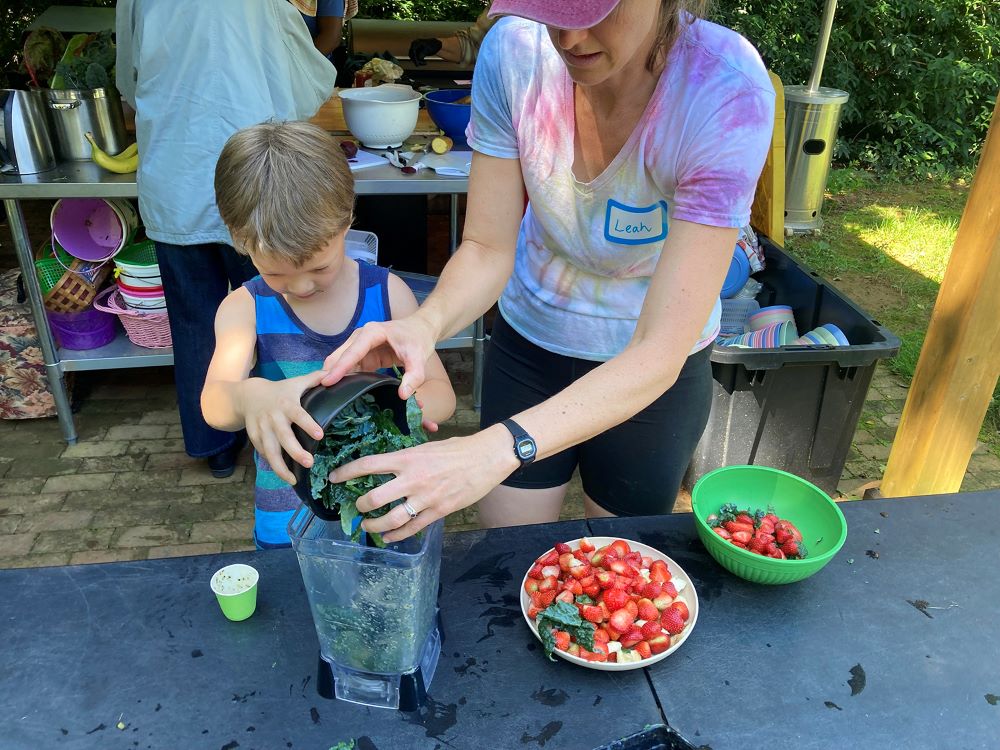 Grow It organizer Leah Reichardt-Osterkatz, right, helps children make smoothies from strawberries they picked, plus kale grown on the farm, at Spring Forest in Hillsborough, North Carolina, on Wednesday, May 29, 2024. (RNS photo/Yonat Shimron)