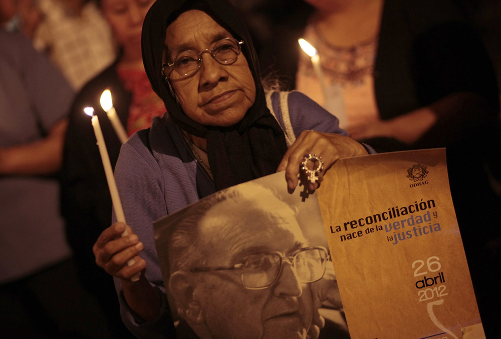 A woman holds a candle and a sign with an image of Auxiliary Bishop Juan Gerardi Conedera outside St. Sebastian Church April 26, 2012, to commemorate the 14th anniversary of his death in Guatemala City. (CNS/Reuters/Jorge Dan Lopez) 