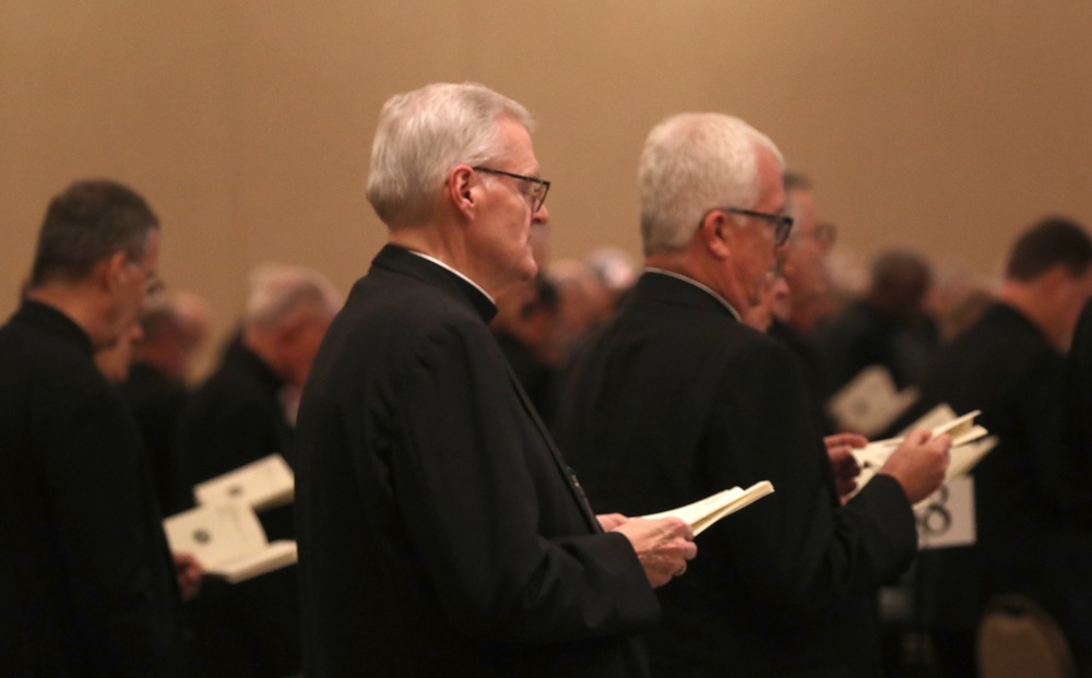 Bishops stand together, praying from bulletins