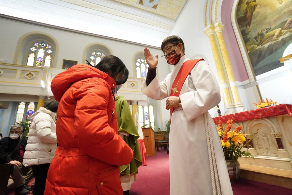 Deacon, vested, makes sign of cross over woman with head bowed.