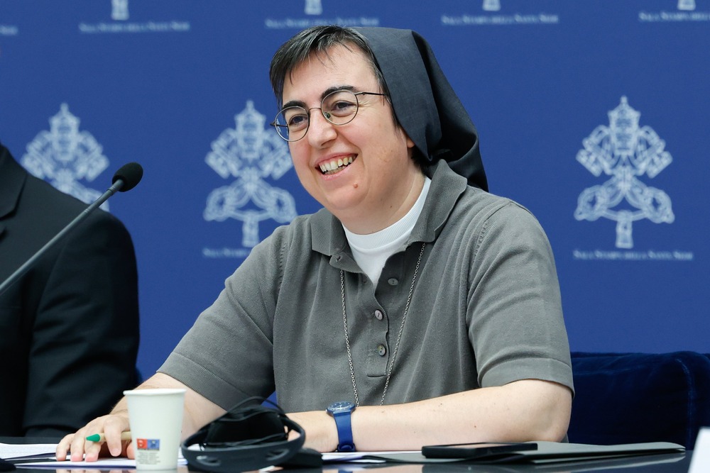 Sister Smerilli smiles as she sits and listens at panel desk. 