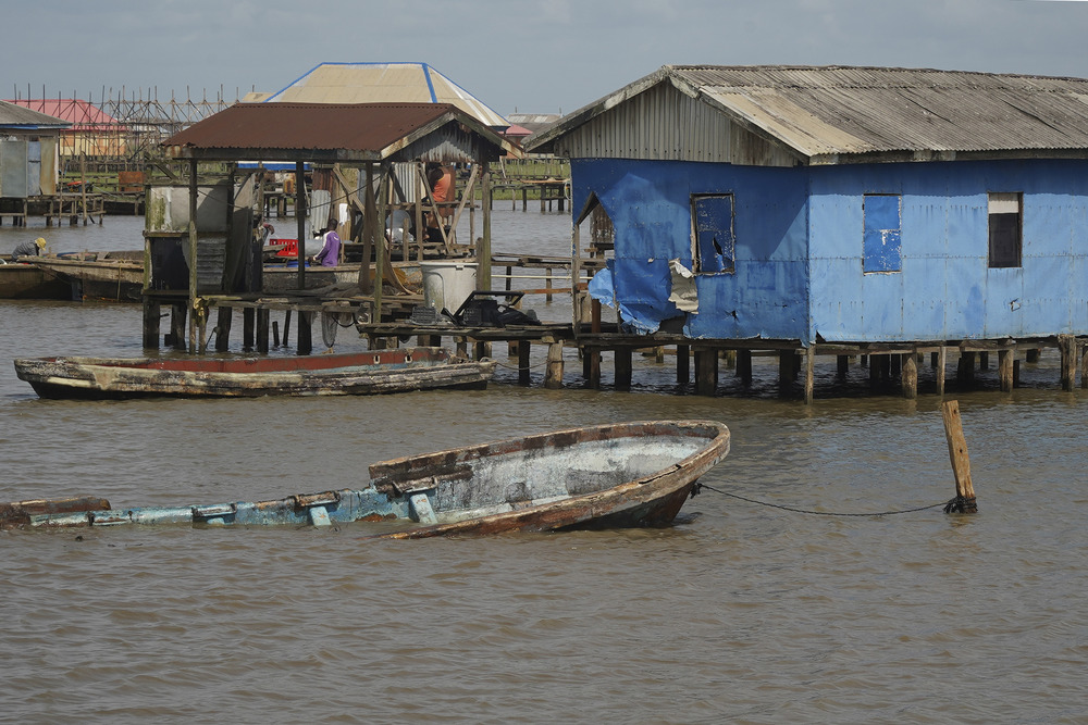 In background are houses on stilts, sitting just barely above the water line, and foregrounded is a partially submerged boat tied to dock. 