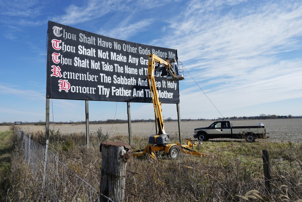 Billboard in field pictured against wide, blue sky. 