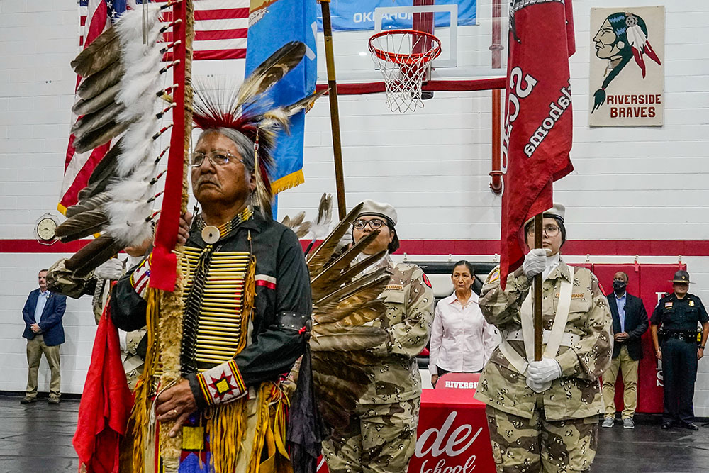 James Nells, of the Navaho Tribe, and a teacher at Riverside Indian School, leads the Riverside Indian School color guard during opening ceremonies July 9, 2022, in Anadarko, Oklahoma, for a meeting to allow U.S. Secretary of the Interior Deb Haaland, rear, to hear about the painful experiences of Native Americans who were sent to government-backed boarding schools designed to strip them of their cultural identities. (AP/Sue Ogrocki, File)