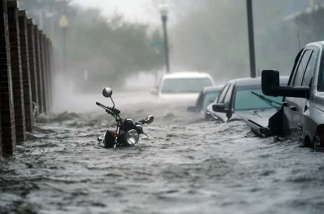 Flood waters rush through nearly submerged vehicles in street