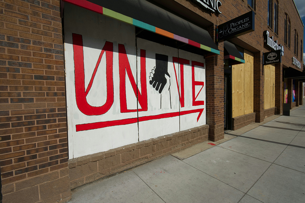 A white sign with clasped hands and the word UNITE in red on the side of a building (Unsplash/Priscilla Gyamfi)