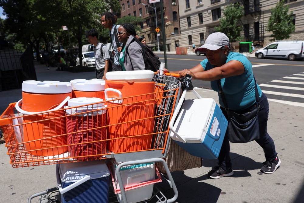 Woman pushes shopping cart filled with large coolers. 