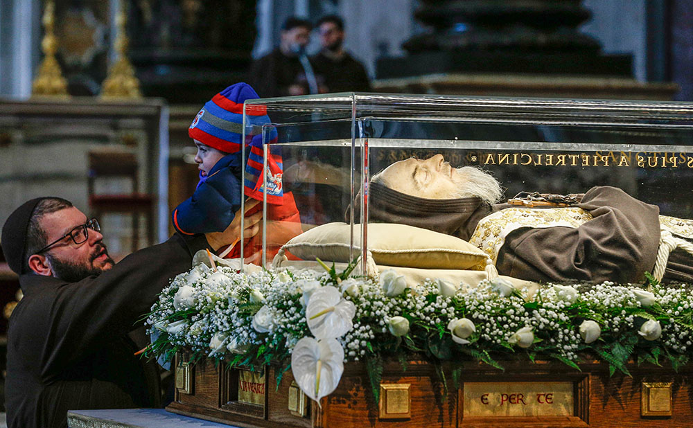 A child is lifted to come into contact with the glass case containing the body of St. Padre Pio in St. Peter's Basilica at the Vatican Feb. 6, 2016. Pio's body was brought to Rome at the request of Pope Francis for the Year of Mercy. (CNS/Paul Haring)