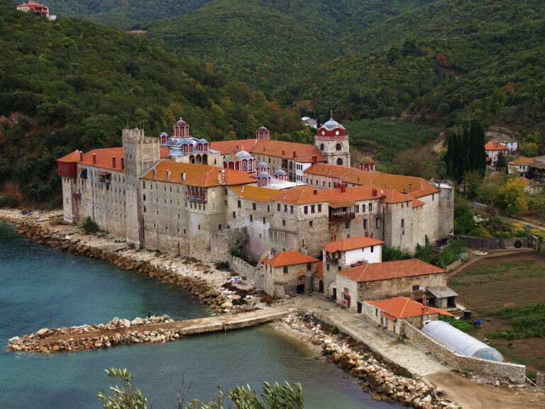 Large, ancient complex sits next to blue, sparkling lake or bay. 