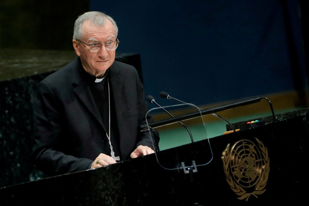 Parolin wearing black clerics stands at podium.