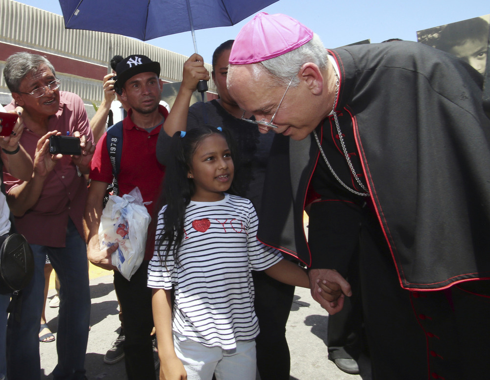 Seitz in purple-piped cassock and purple zucchetto, bends down to take little girl's hand. 