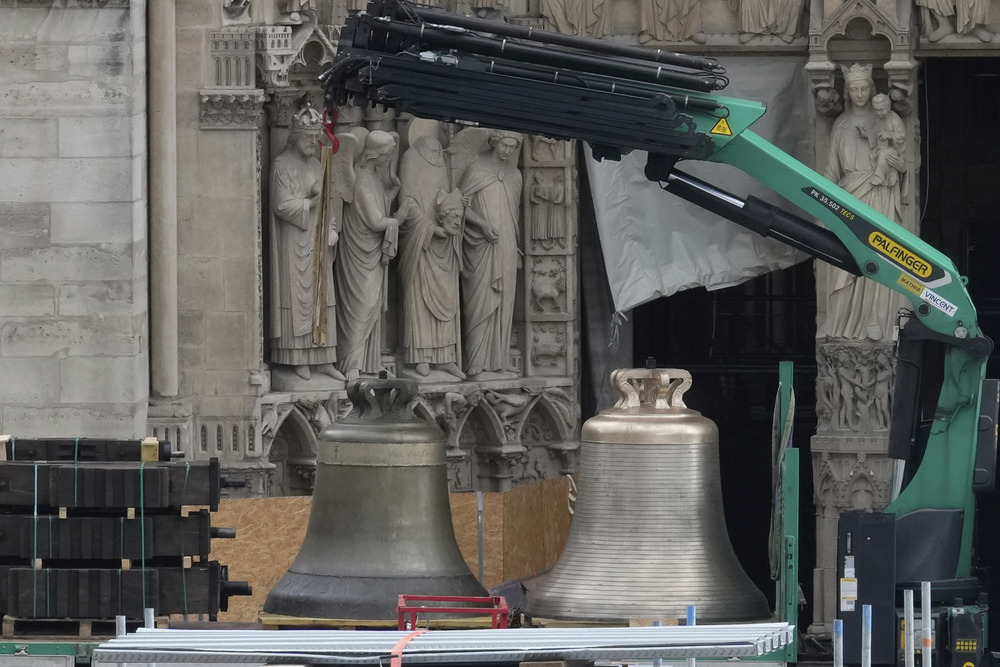 Large bronze bells on truck bed; in background is ornately carved portion of Cathedral exterior. 