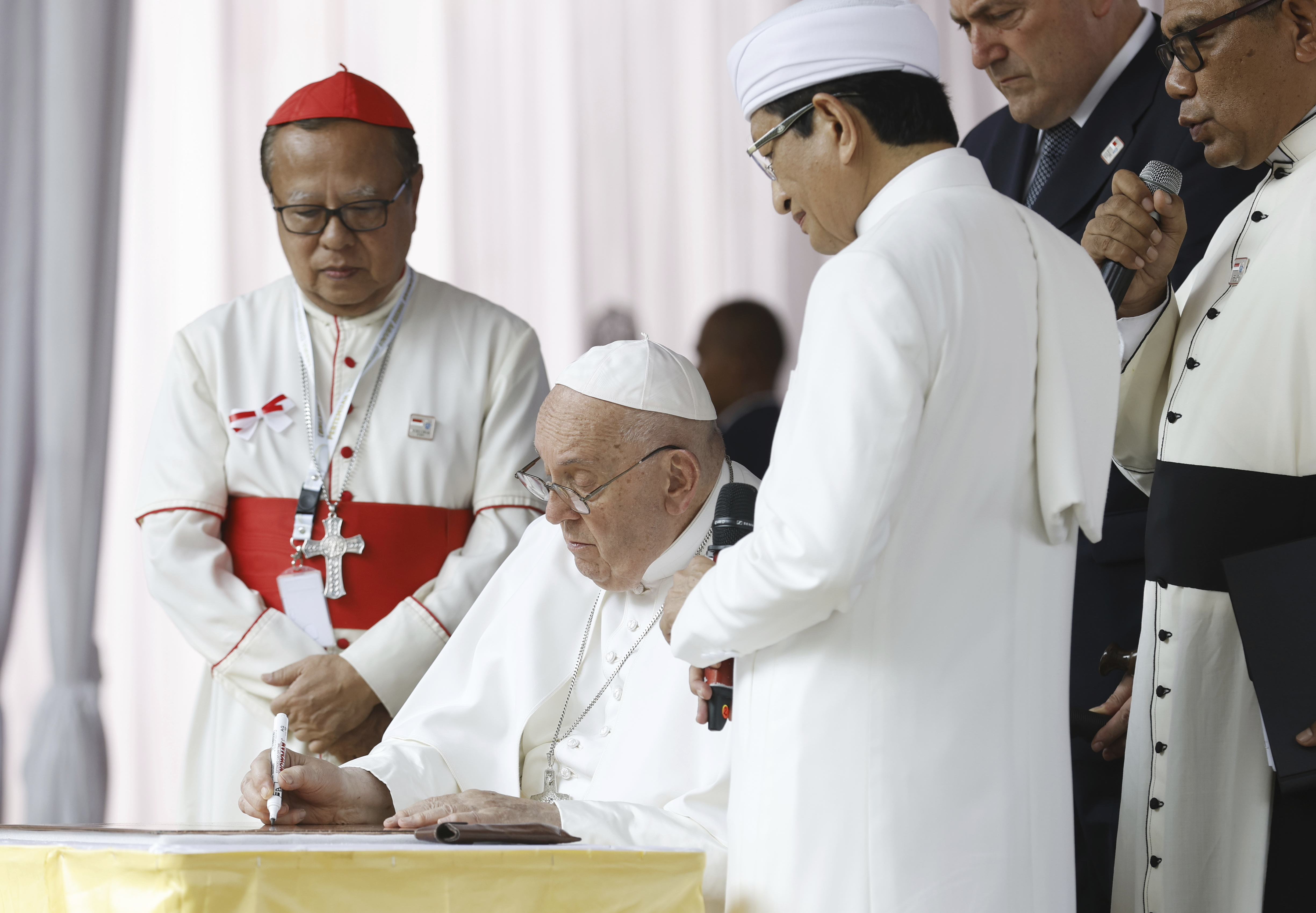 Pope Francis, center, flanked by the grand imam of Istiqlal Mosque Nasaruddin Umar, second right, and Archbishop of Jakarta Cardinal Ignatius Suharyo, left, signs a plate as he arrives at the Istiqlal Mosque for an interreligious meeting in Jakarta Thursday, Sept. 5, 2024. (Mast Irham/Pool Photo via AP)