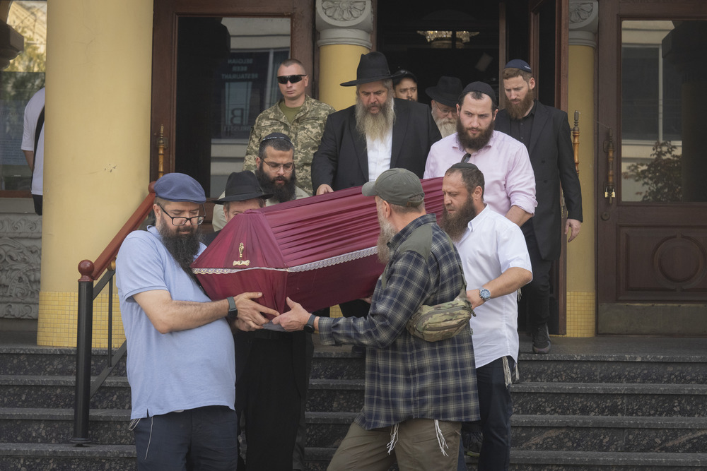 Azman follows pallbearers who gingerly carry coffin down exterior steps of synagogue.