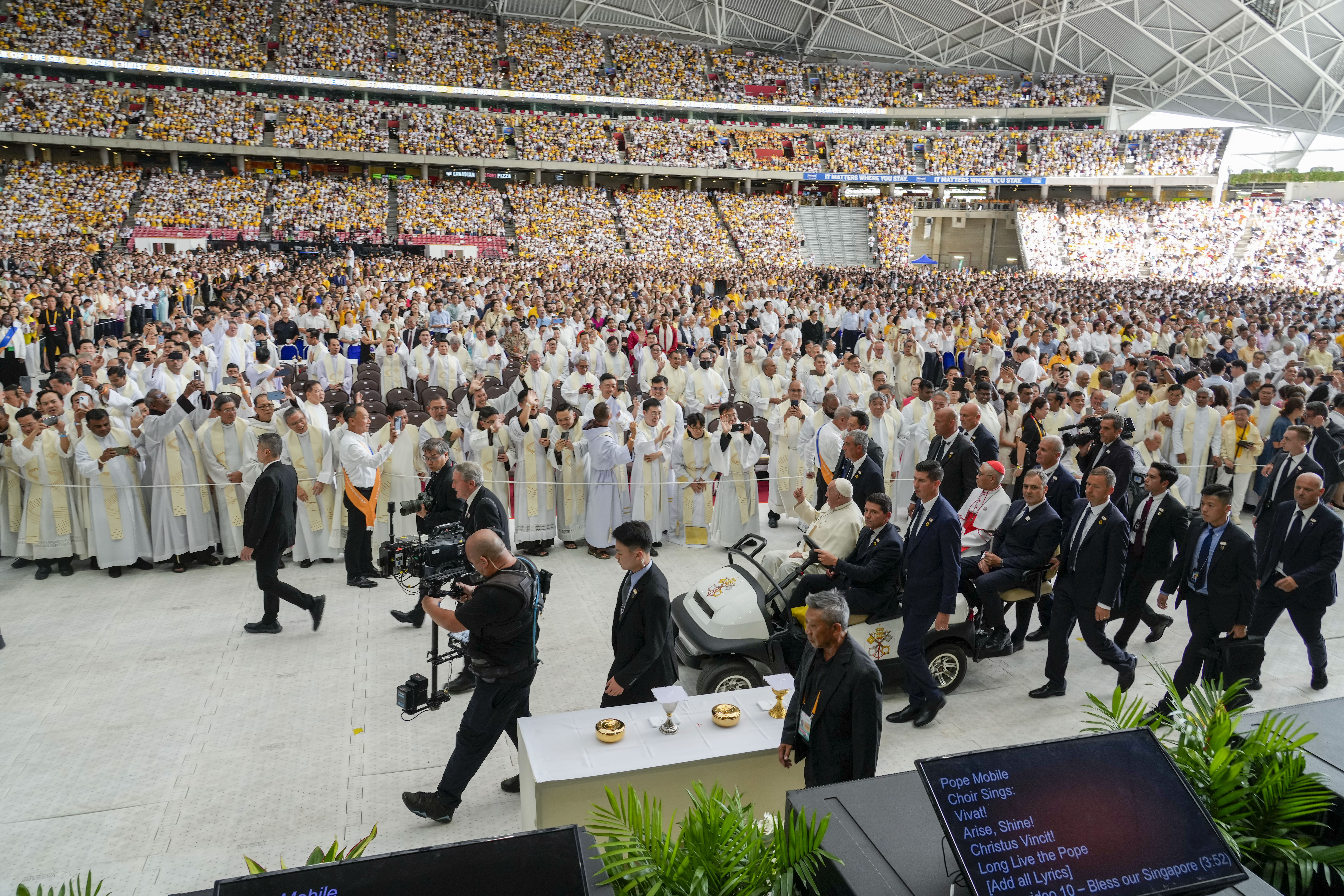 Faithful wait in the Singapore SportsHub National Stadium where Pope Francis will preside over a Mass "In Memory of the Most Holy Name of Mary" celebrated by the archbishop of Singapore, Cardinal William Goh Seng Chye, center right, Thursday, Sept. 12. Pope Francis has praised Singapore's economic development as a testament to human ingenuity. But he is urging the city-state to look after the weakest too. Francis made the remarks Thursday on the final leg of the longest and farthest tour of his papacy. (AP 