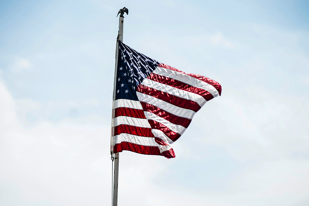 American flag flying against a blue sky with some white clouds (Unsplash/Andre Hunter)