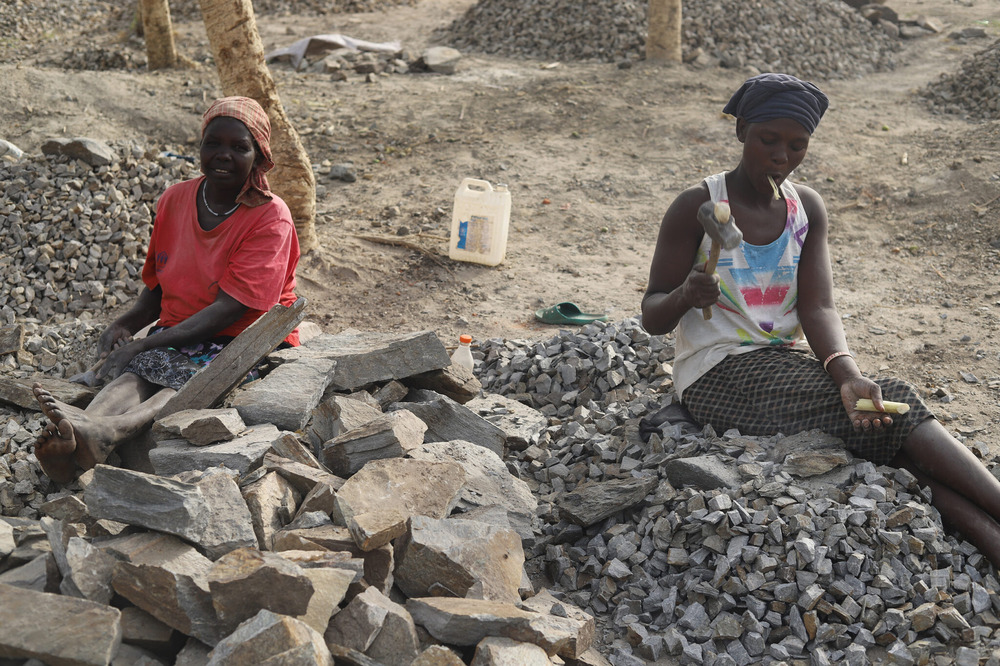 Two women sit on a pile of rocks holding mallets.