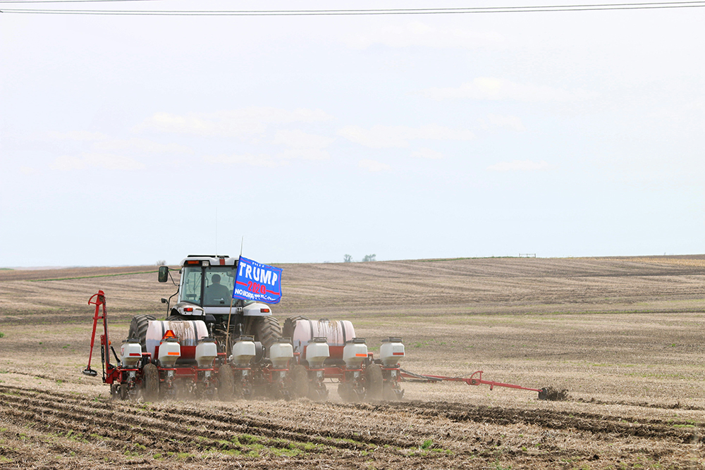 A combine plows a field with a Trump flag flying (Unsplash/Laura Seaman)