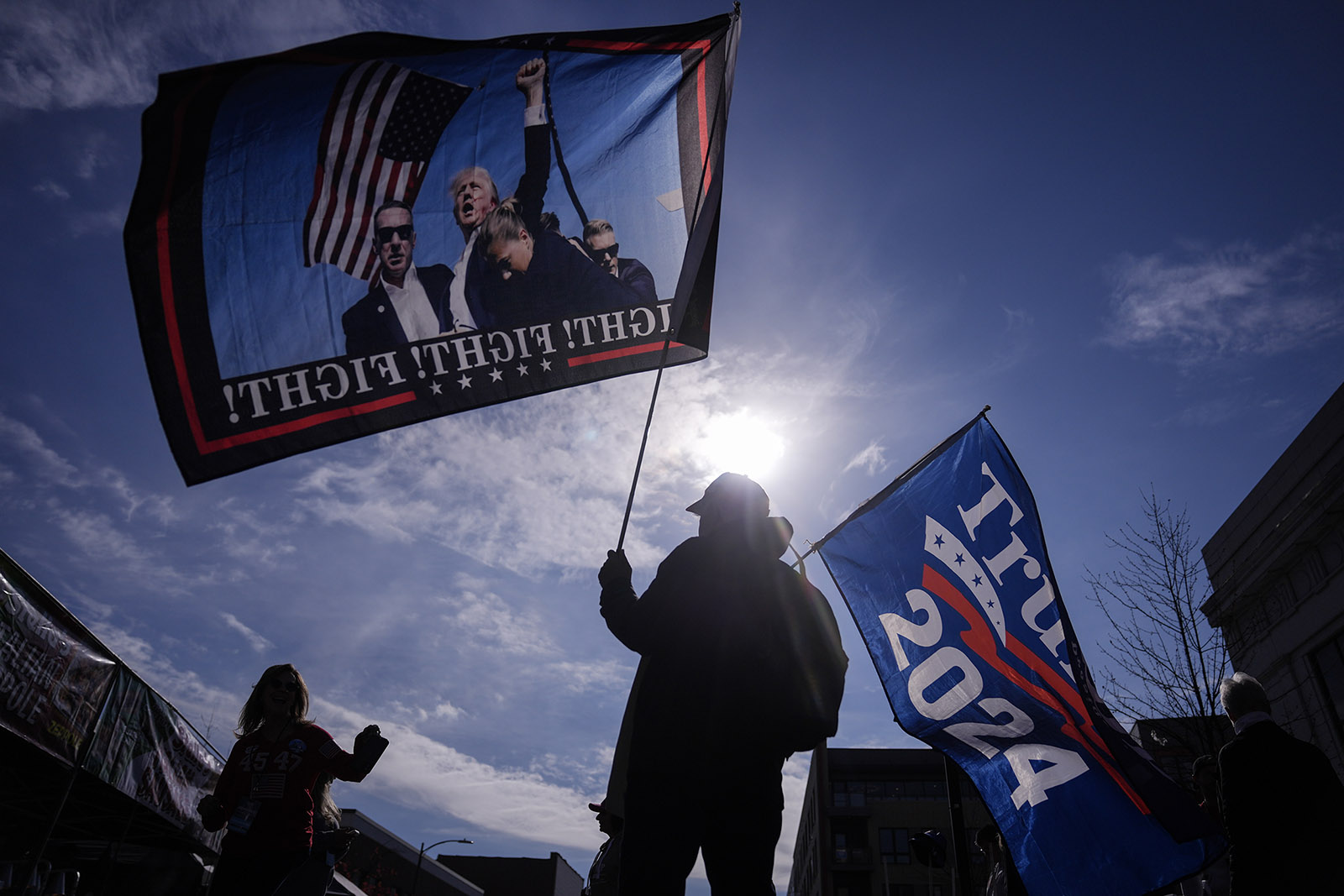 People holding Trump flags silhouetted against bright sun. 