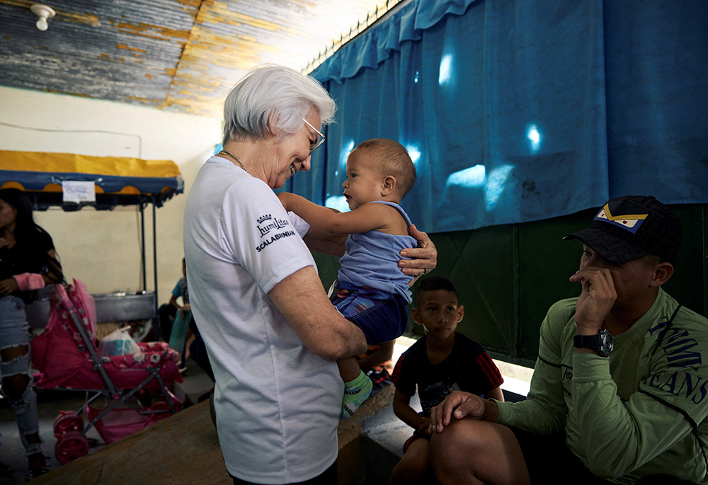 Scalabrinian Sr. Rosita Milesi, recipient of the 2024 Nansen Refugee Award from the Office of the United Nations High Commissioner for Refugees, holds Alexander Solis and greets Venezuelan refugees and migrants as they wait to collect donated hygiene and nutrition kits at the Casa de Acolhida Sao Jose, a temporary shelter for refugees and migrants in Pacaraima, Brazil, on Aug. 24. (UNHCR/Marina Calderon/Handout via Reuters)