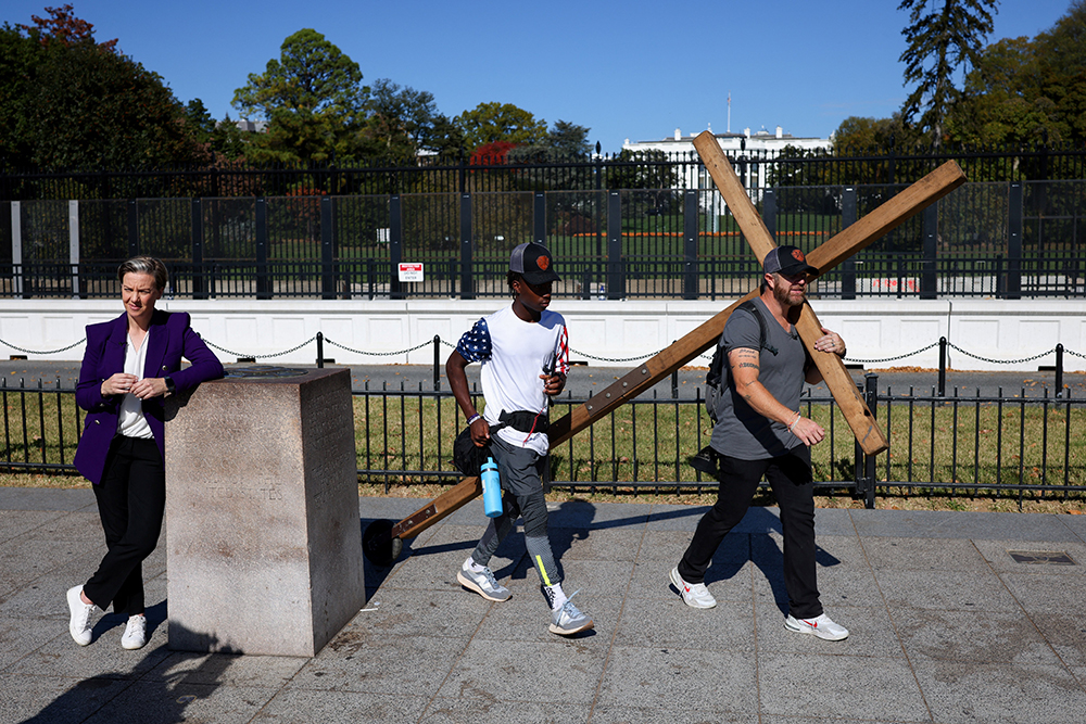 A man wheels a large wooden cross near the White House in Washington as a reporter records a broadcast during the U.S. presidential election on Nov. 5, 2024, Election Day. (OSV News/Reuters/Daniel Cole)