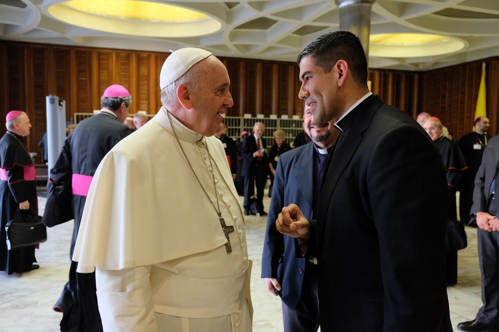 Francis and Dorantes face each other smiling in conversation. 