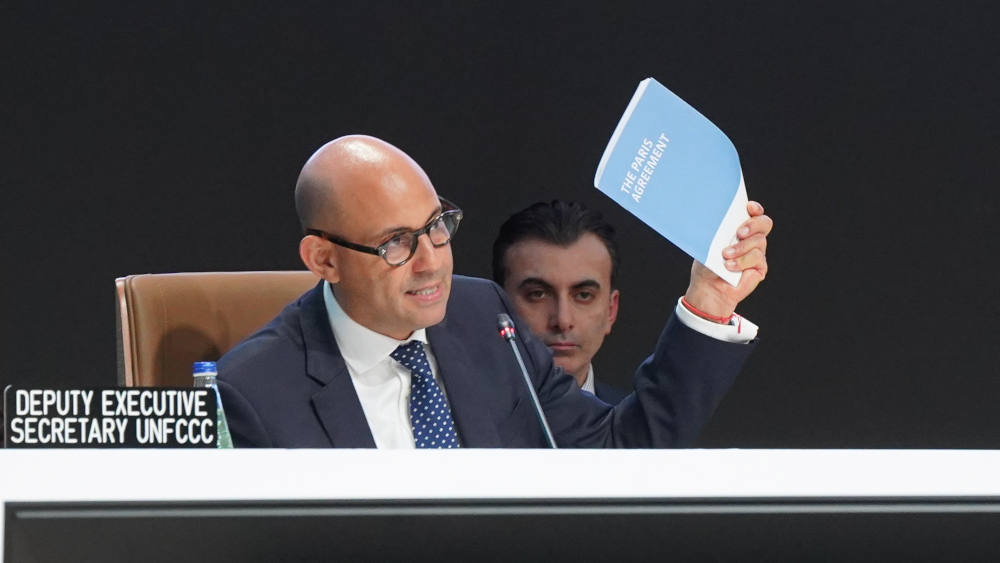 Simon Stiell, executive secretary of the United Nations Framework Convention on Climate Change, waves a copy of the Paris Agreement as he addresses the closing plenary of COP29 on Nov. 24 in Baku, Azerbaijan. (UN Climate Change/Lucia Vasquez-Tumi)