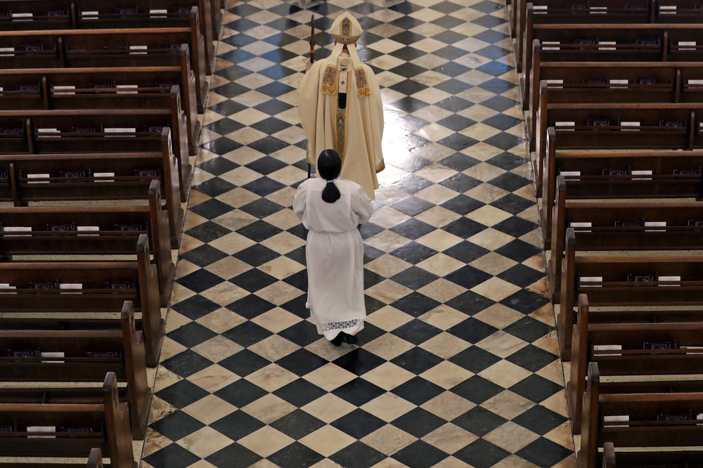 Vested archbishop processes through aisle followed by acolyte.