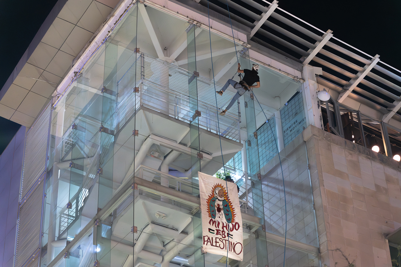 Person on rope against tall building, banner hangs.