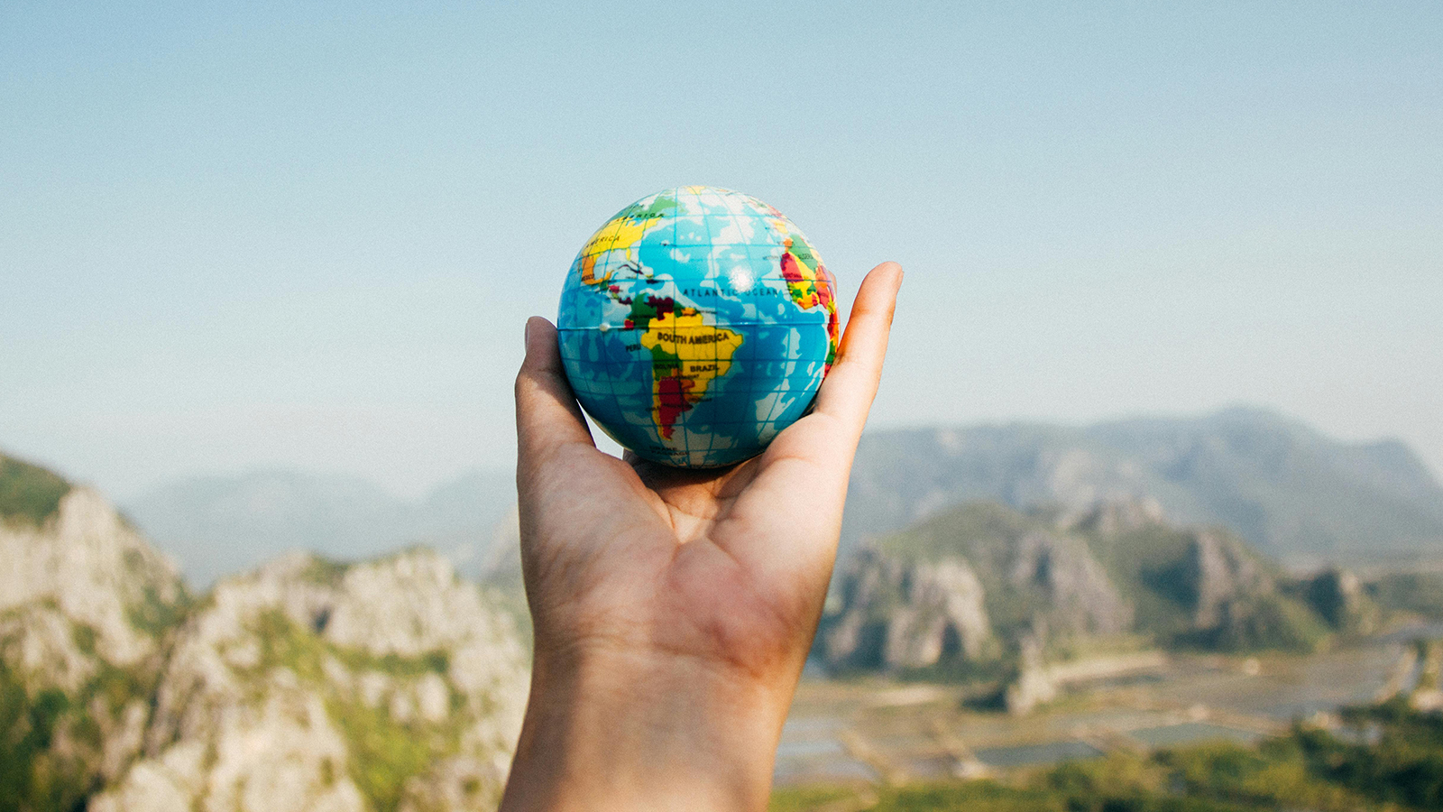 hand holding globe with mountains in the background