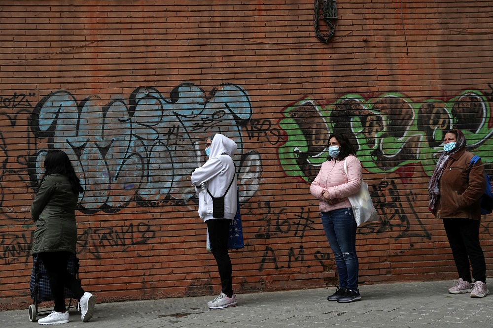 People in masks wait in line to receive donated food